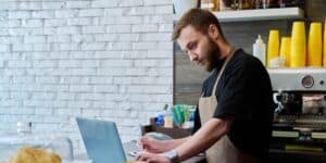 A coffee shop owner is doing work on a laptop