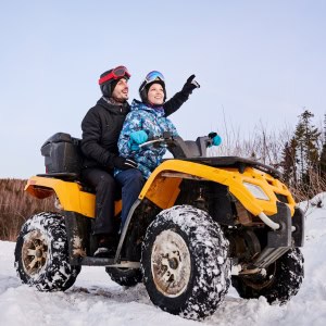 A man and woman wearing snow gear are sitting on a snowmobile