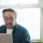 A man wearing glasses is looking at his laptop