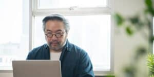 A man wearing glasses is looking at his laptop