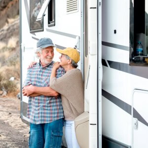 A mature couple standing outside of their fifth wheel on vacation