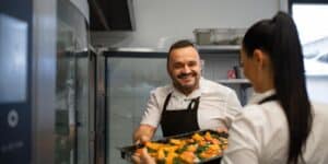 A restaurant owner passing a tray of food to a staff member in the kitchen