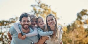 A smiling family of four is standing in a park