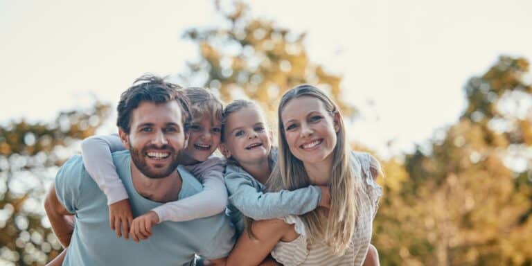 A smiling family of four is standing in a park