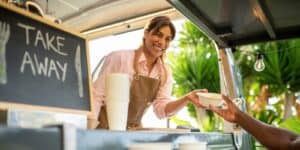 A woman is handing food to a customer from her food truck