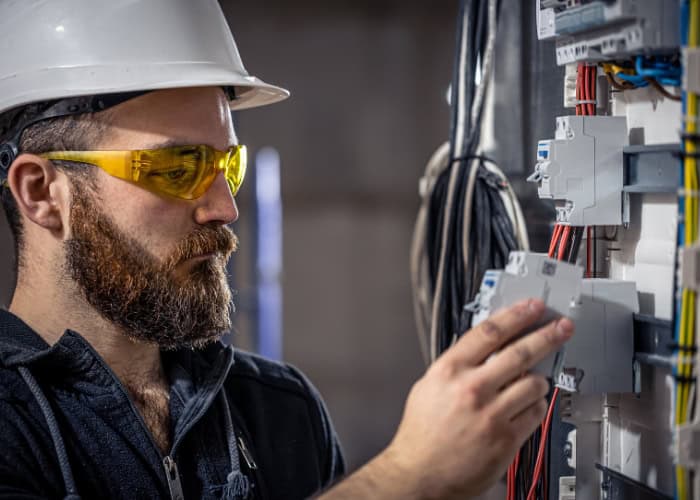 An electrician wearing safety gear is inspecting wires