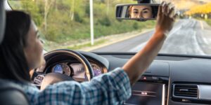 A woman is driving a car and smiling in the rear view mirror.