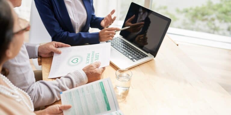 Insurance agent meeting with a couple while looking at a laptop and insurance policy documents