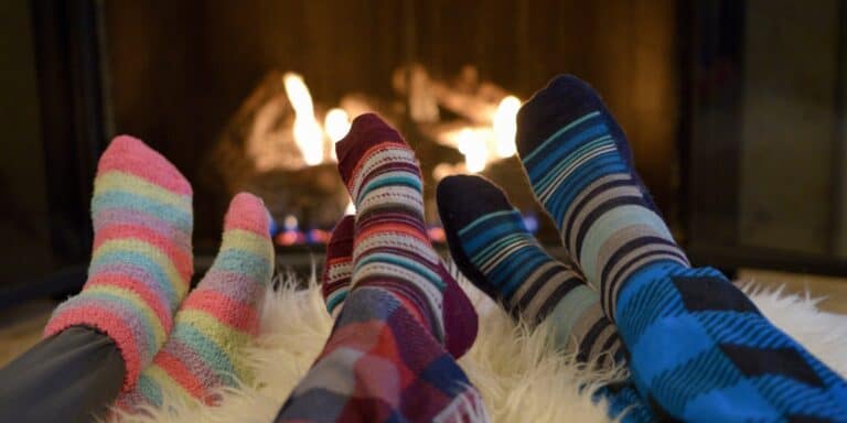 Three people are sitting near the fireside with colorful pajamas and socks on.
