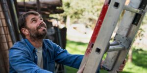 A man is holding a ladder steady and looking upwards.