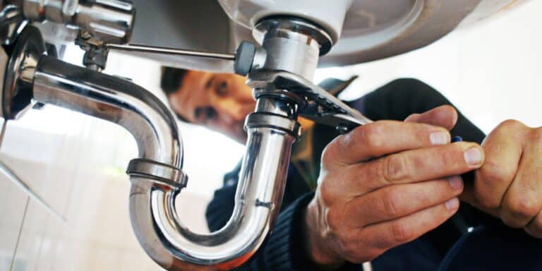 Close up image of a plumber completing a repair on a sink pipe.