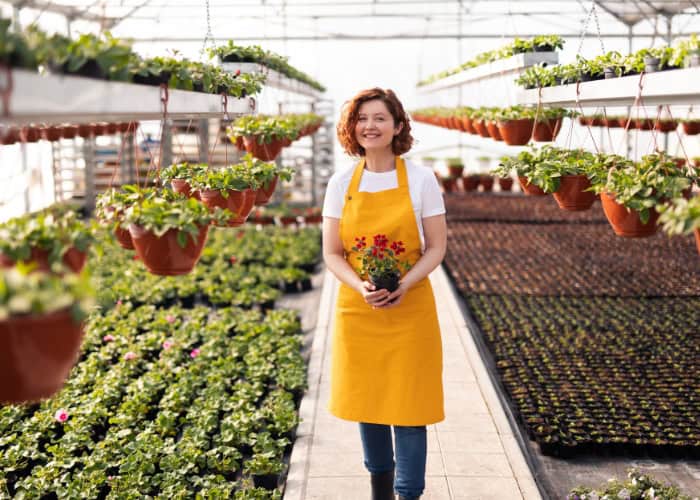 a woman wearing an apron is holding flowers in a greenhouse